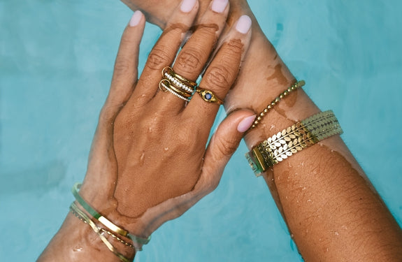 Gold Teardrop Bangle, worn on a wrist with gold rings, hoop earring and necklaces