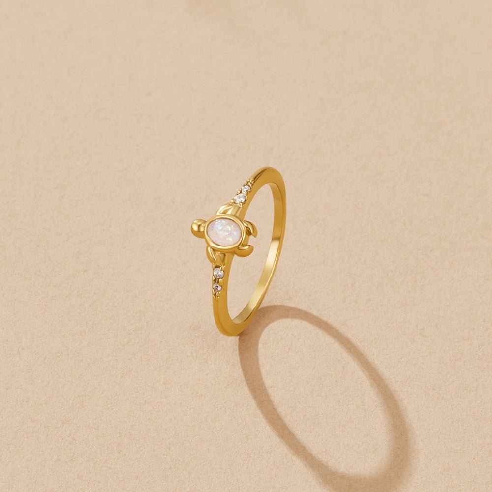 Opal Gold Turtle Ring, gold ring with turtle motif and pale opal, on beige surface